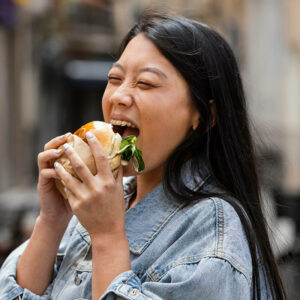 happy asian woman eating burger outdoors
