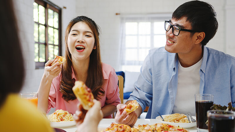happy young friends group having lunch home asia family party eating pizza food laughing enjoying meal while sitting dining table together house celebration holiday togetherness (2)